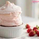 Gordon Ramsay raspberry soufflé risen tall above a white ramekin, dusted with icing sugar, with dark chocolate lining visible at the rim and fresh raspberries on the side