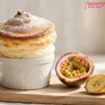 Passion fruit soufflé risen tall above its ramekin, dusted with powdered sugar and golden on top, with halved passion fruit nearby