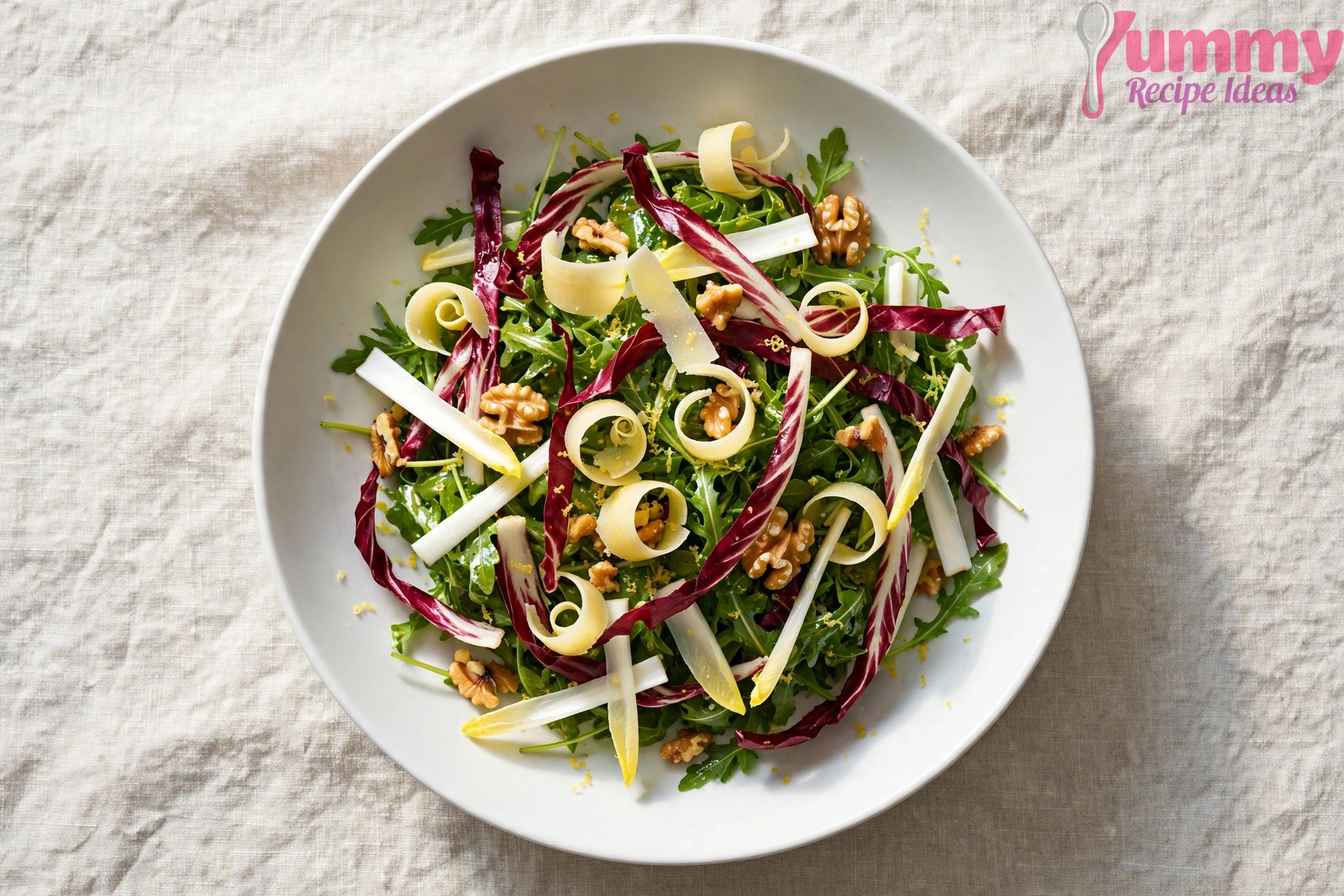 Overhead view of Italian rocket salad with arugula, radicchio, endive, toasted walnuts, and shaved Parmesan in a white bowl